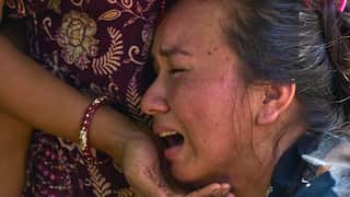 A woman in a blue shirt cries as another person with a beaded bracelet on their wrist cradles her head in their hands.