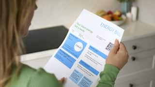 A woman in a green jumper looks at a paper electricity bill.