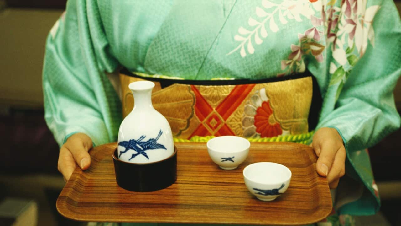 Mid section view of a woman holding saki on tray, Japan