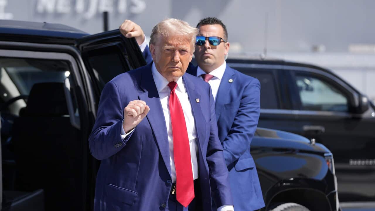Donald Trump, in blue and tie, is standing next to his car.