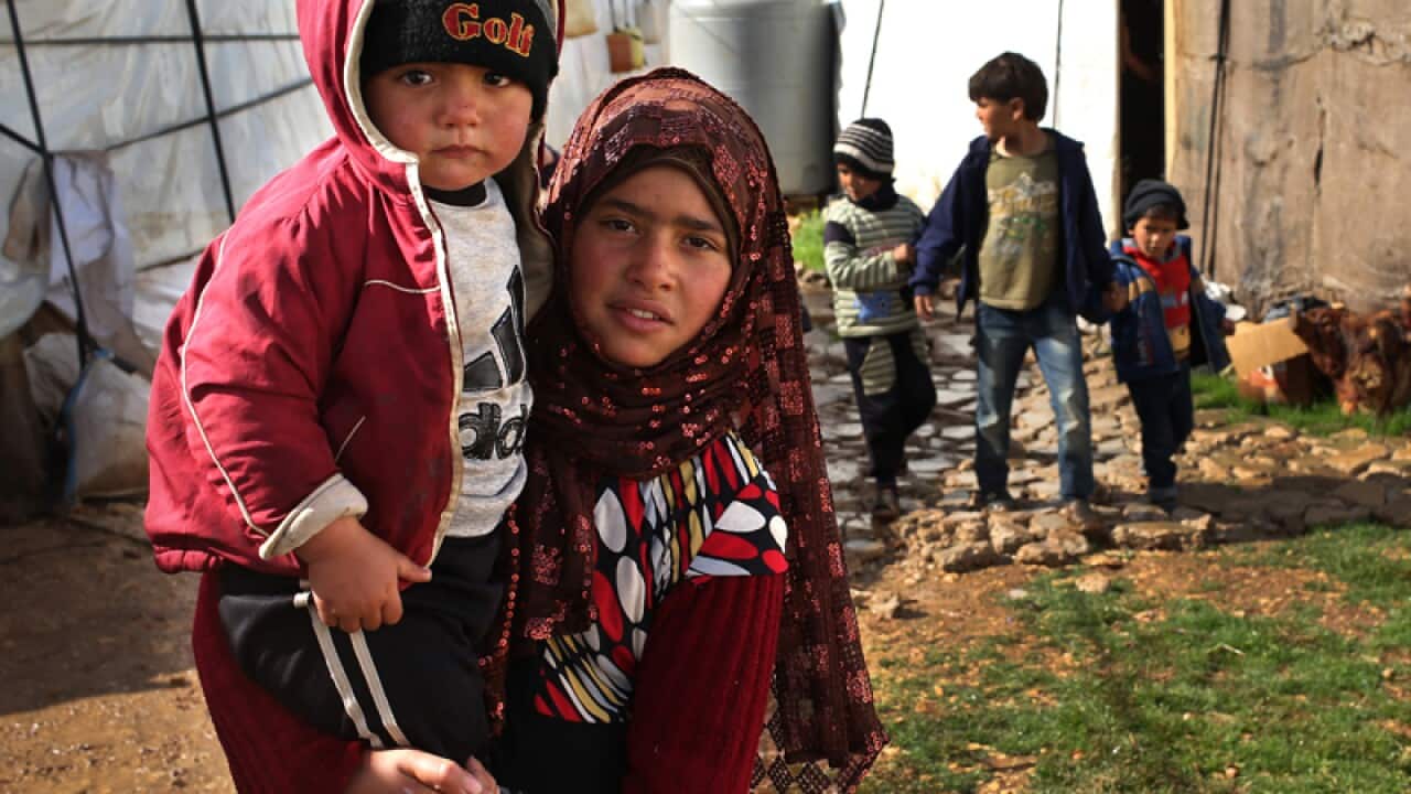 A displaced Syrian girl, foreground, carries her brother, Lebanon