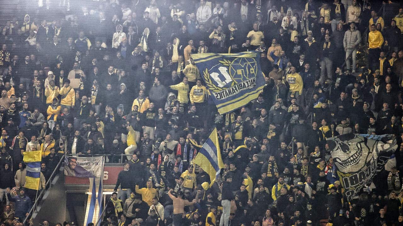 Supporters of the Maccabi Tel Aviv football club in the stands, with some raising flags.