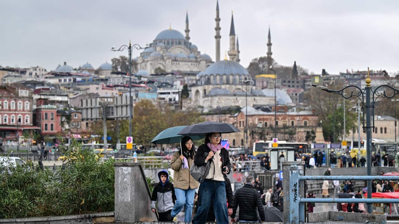 People holding umbrellas as they walk along a street with buildings in the background.