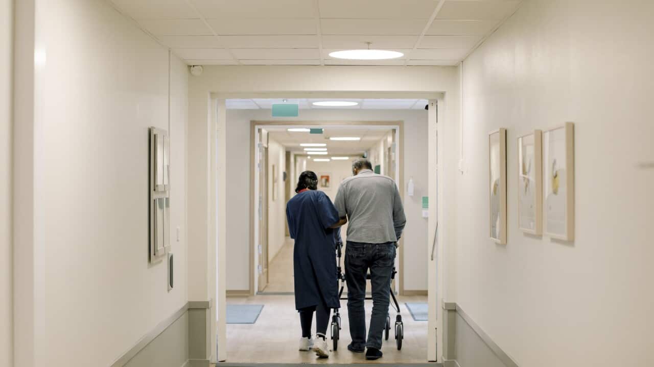 Rear view of female nurse walking with senior man in corridor at nursing home