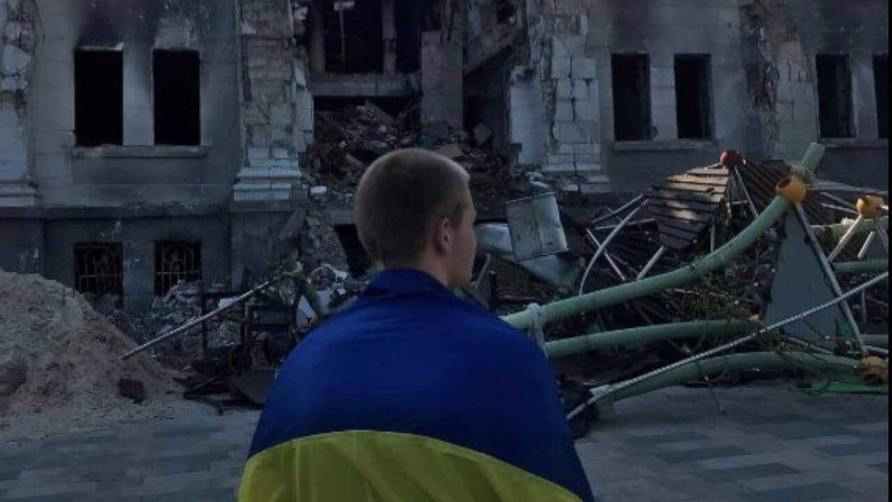 Boy with Ukrainian flag looks at bombed out building.