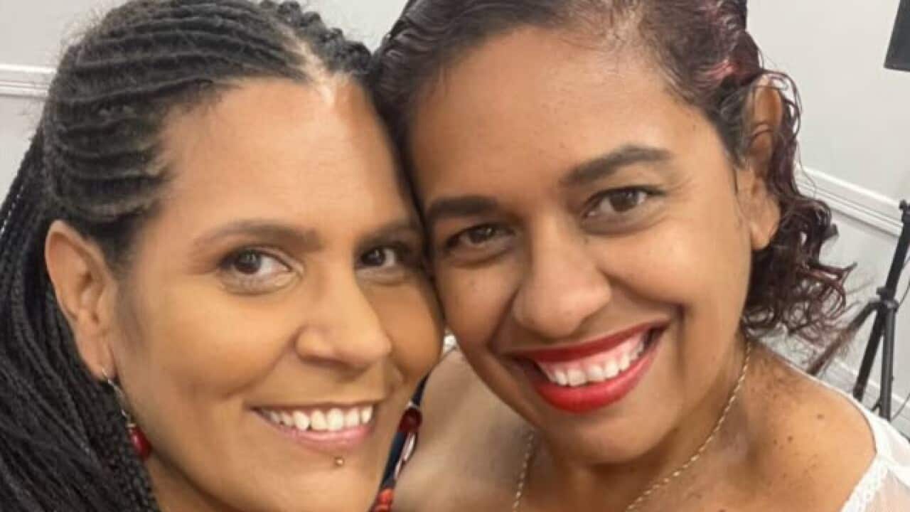 Wwo women standing arm in arm smiling at the camera.