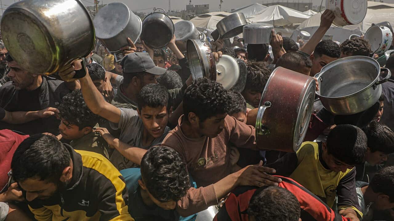A group of tightly-packed people outside, many holding pots
