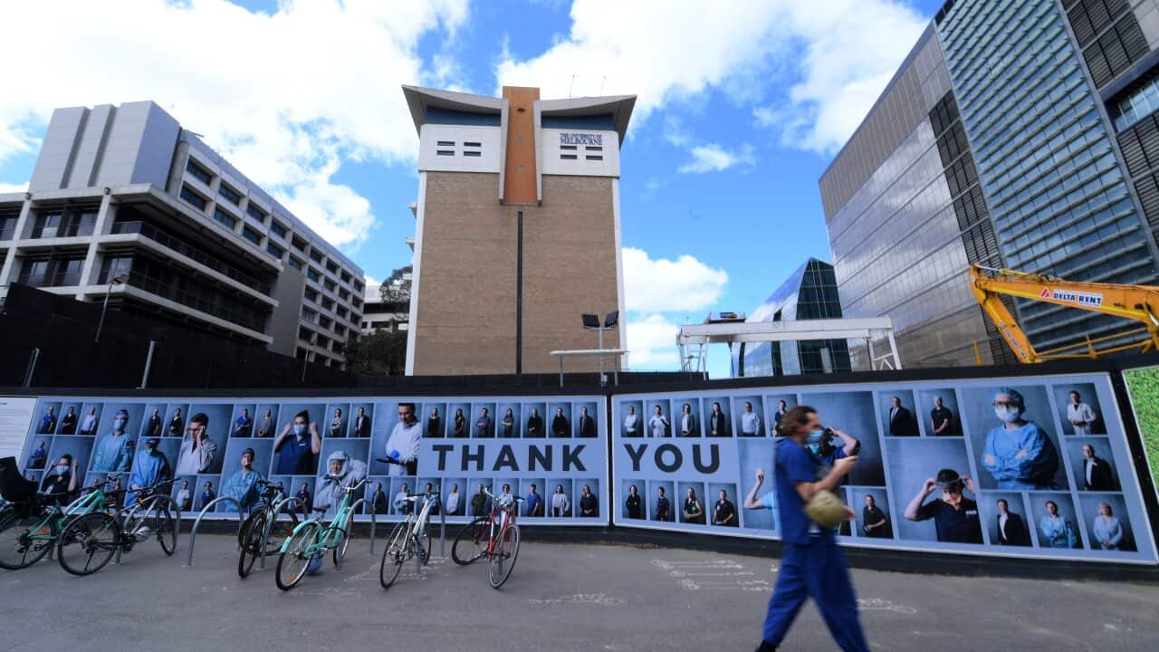 People wearing face masks walk past an outdoor photography exhibition of healthcare workers in Melbourne.