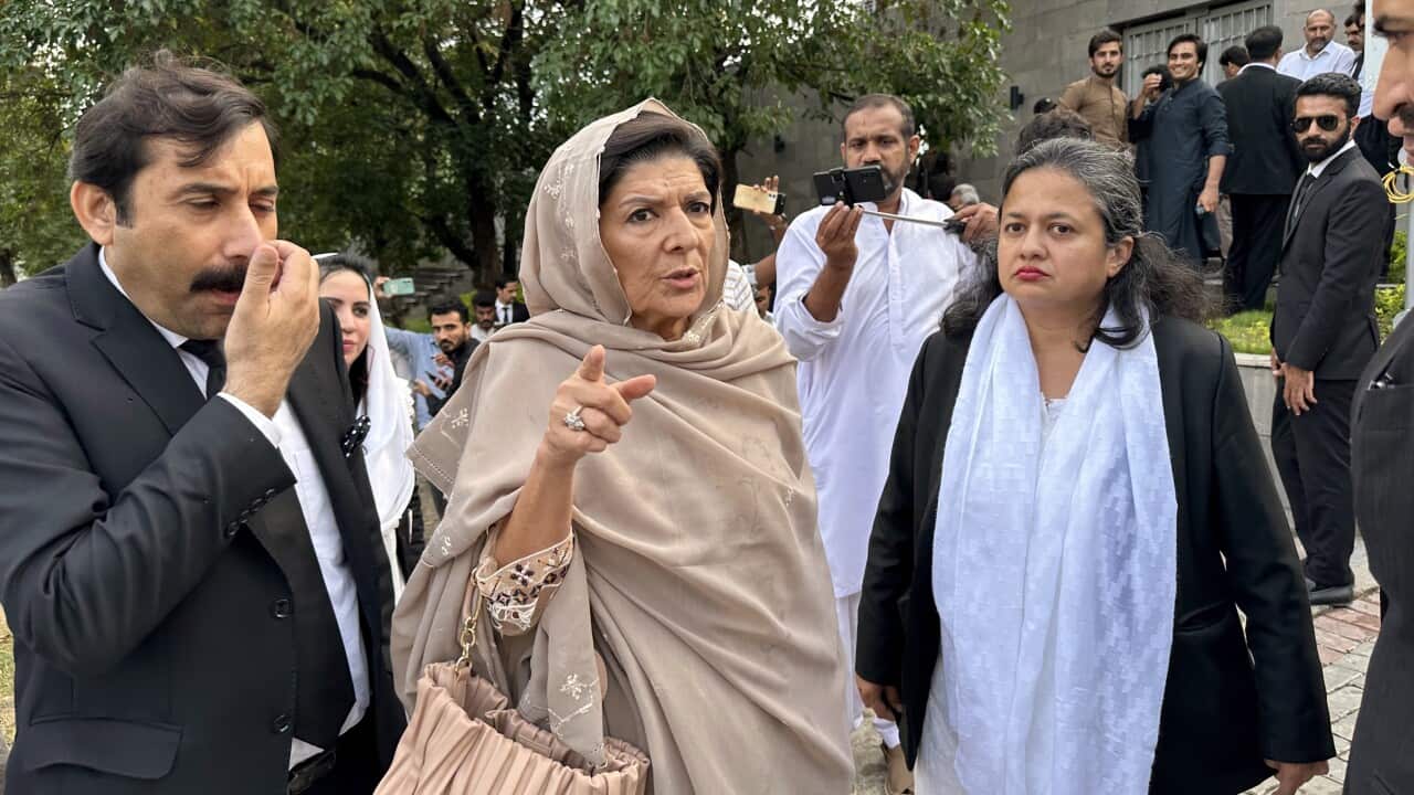 A woman stands pointing as she talks