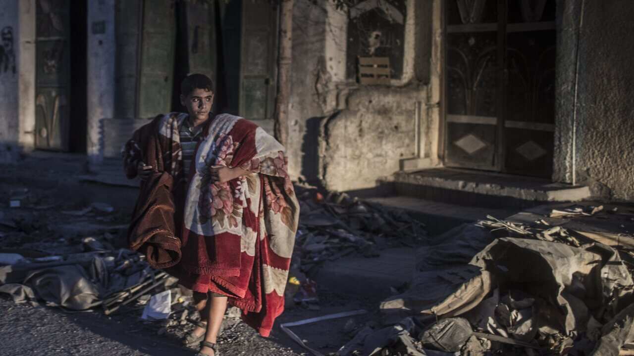 A young Palestinian man carrying blankets trying to leave his home hours before a 72-hours ceasefire between Israel and Hamas will come to an end. (EPA)