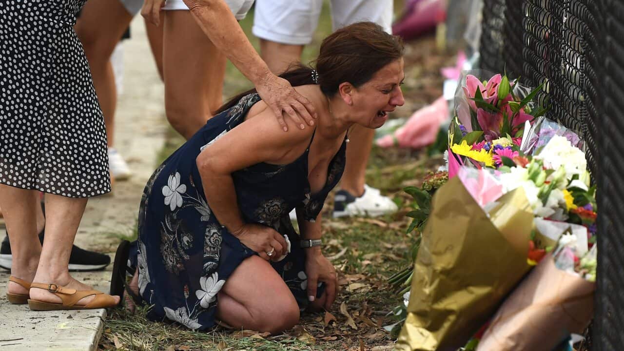 A woman grieves near flowers placed at the scene where seven children were hit on a footpath by a four-wheel drive in the Sydney suburb of Oatlands.