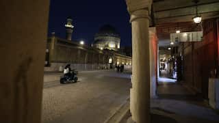 A scooter drives down a cobbled street, viewed through an archway at night