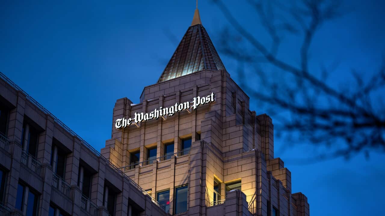 A nighttime shot of a building, topped with a tower-like roof and an illuminated "The Washington Post" logo.
