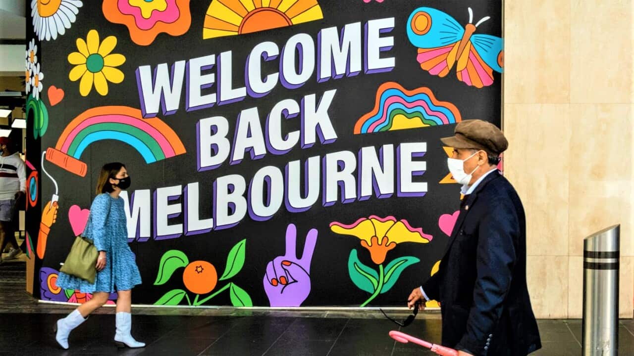 People wearing face masks walk by David Jones windows "Welcome Back Melbourne" at Bourke Street mall during the reopening.