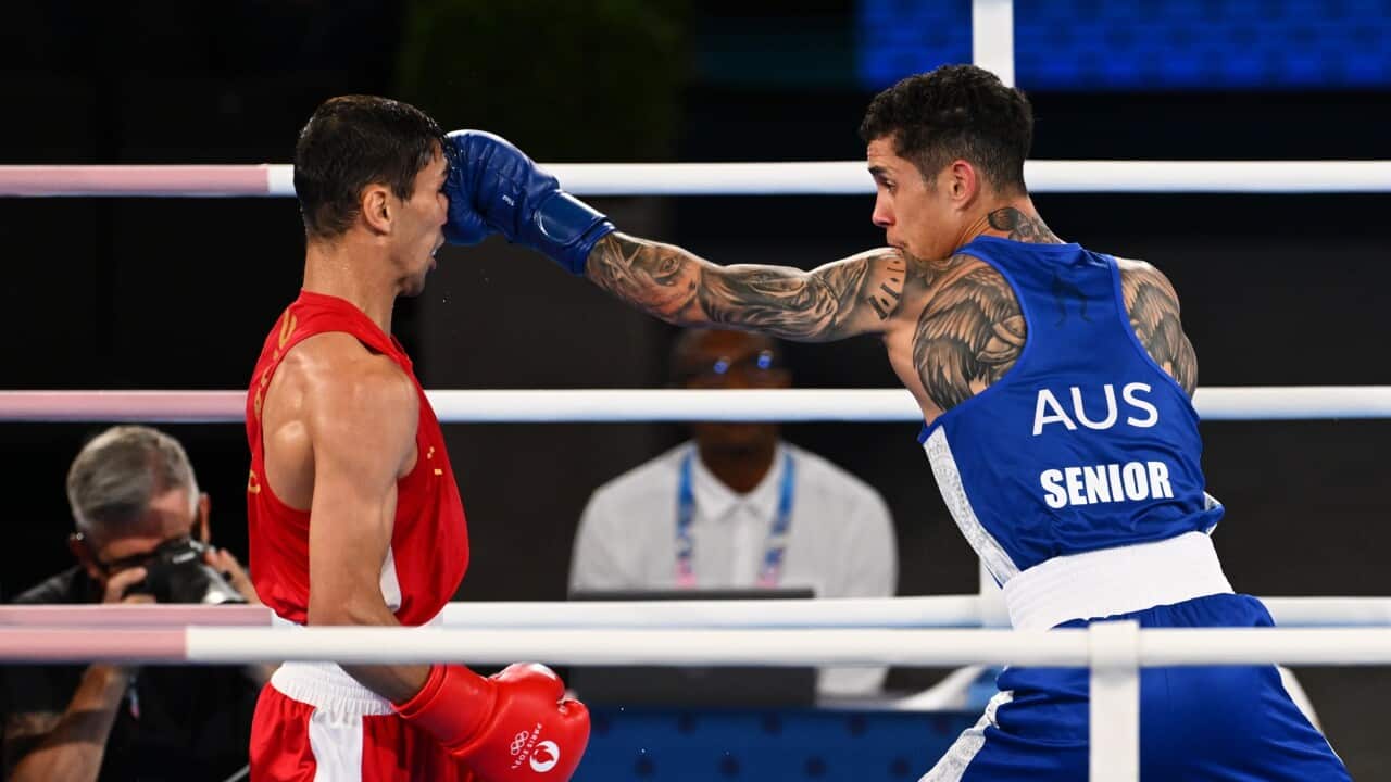 Australian boxer Charlie Senior in blue and Uzbekistani boxer Abdumalik Khalokov in red boxing in a ring. Senior is punching Khalokov in the head.