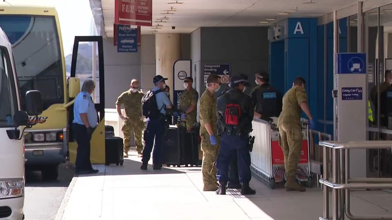 Officials guide returning travellers onto coaches to be taken into quarantine in April