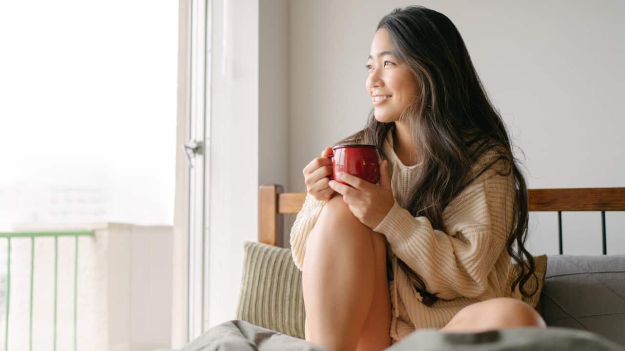 Beautiful young woman drinking hot drink in her bed in the morning