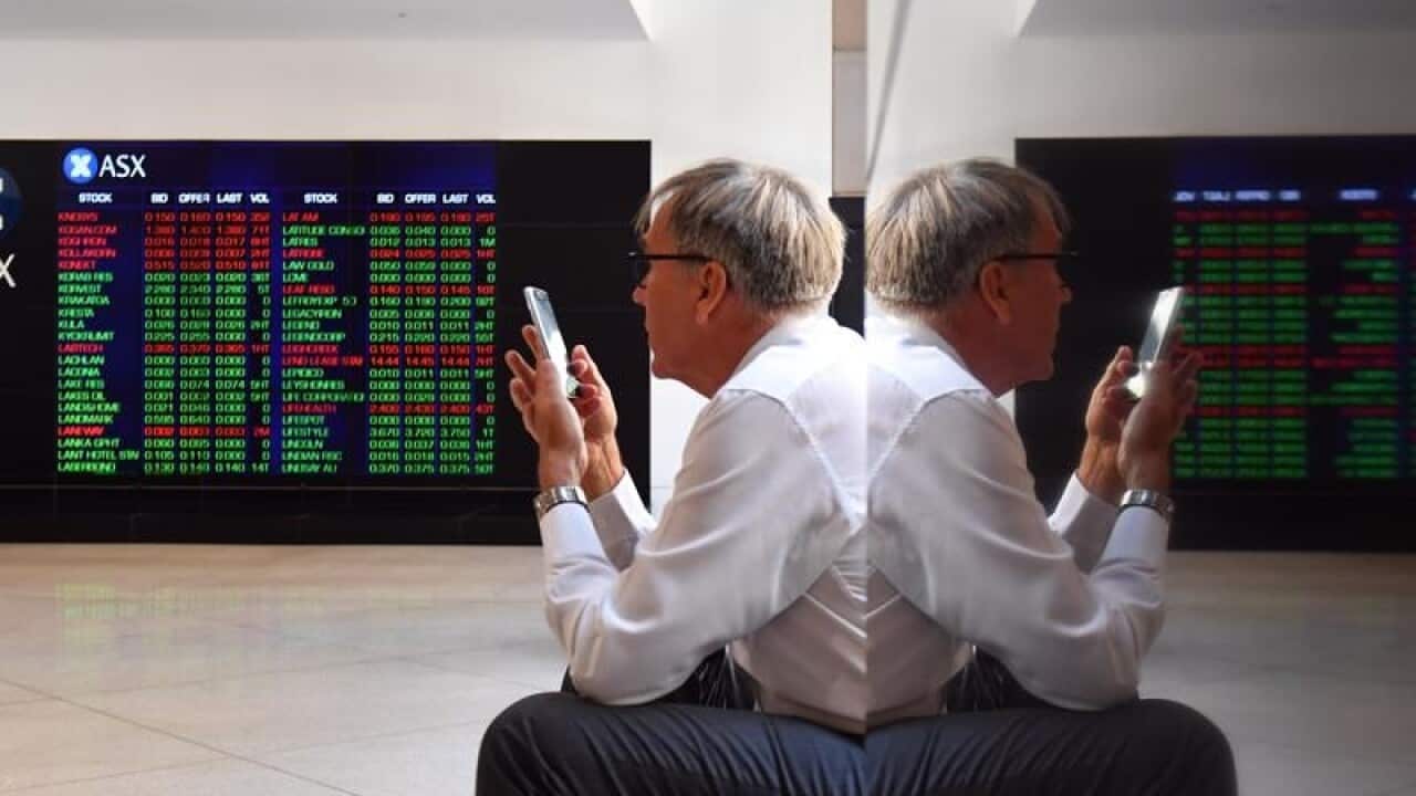 A man using his mobile phone is reflected against a wall at the ASX.