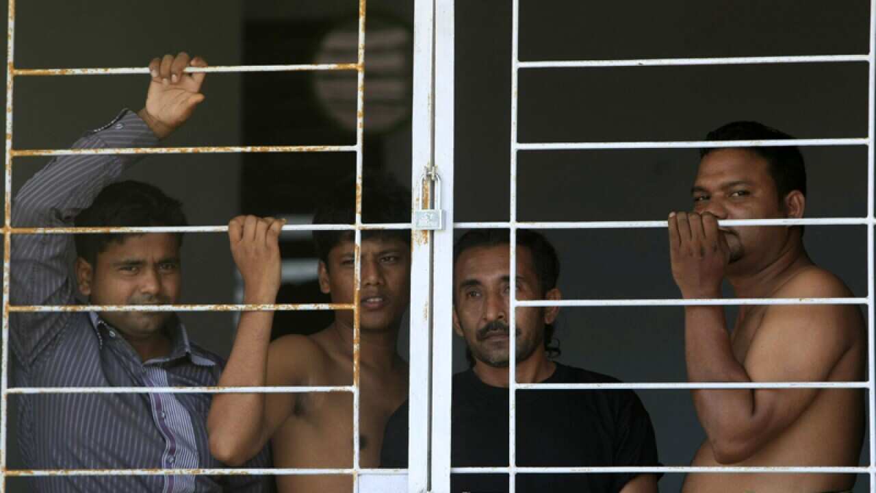 Asylum seekers stand behind bars at temporary shelters