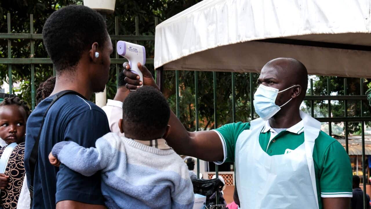 A health official uses a thermometer to screen people in front of Kibuli Muslim Hospital in Kampala, Uganda