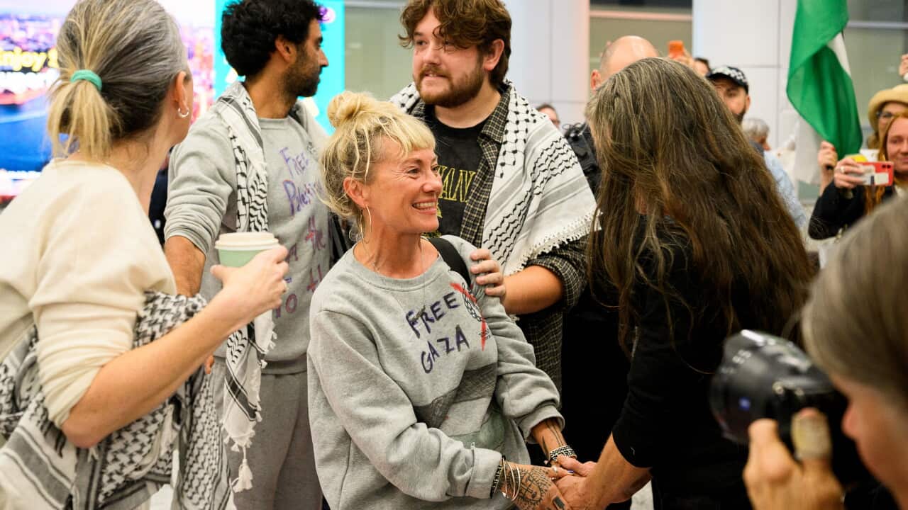 A group of people wearing Palestinian keffiyehs and jumpers saying 'Free Gaza' being greeted at an airport.