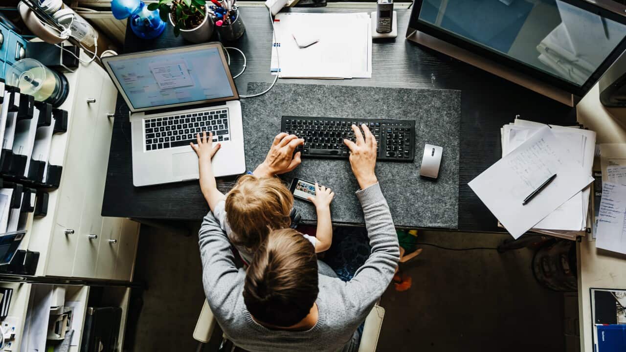 A woman works on her laptop with a young girl sitting on her lap.