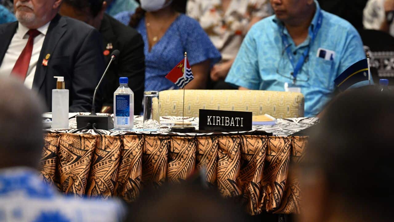 A sign that reads "Kiribati" sits on a desk with no one sitting at the chair.