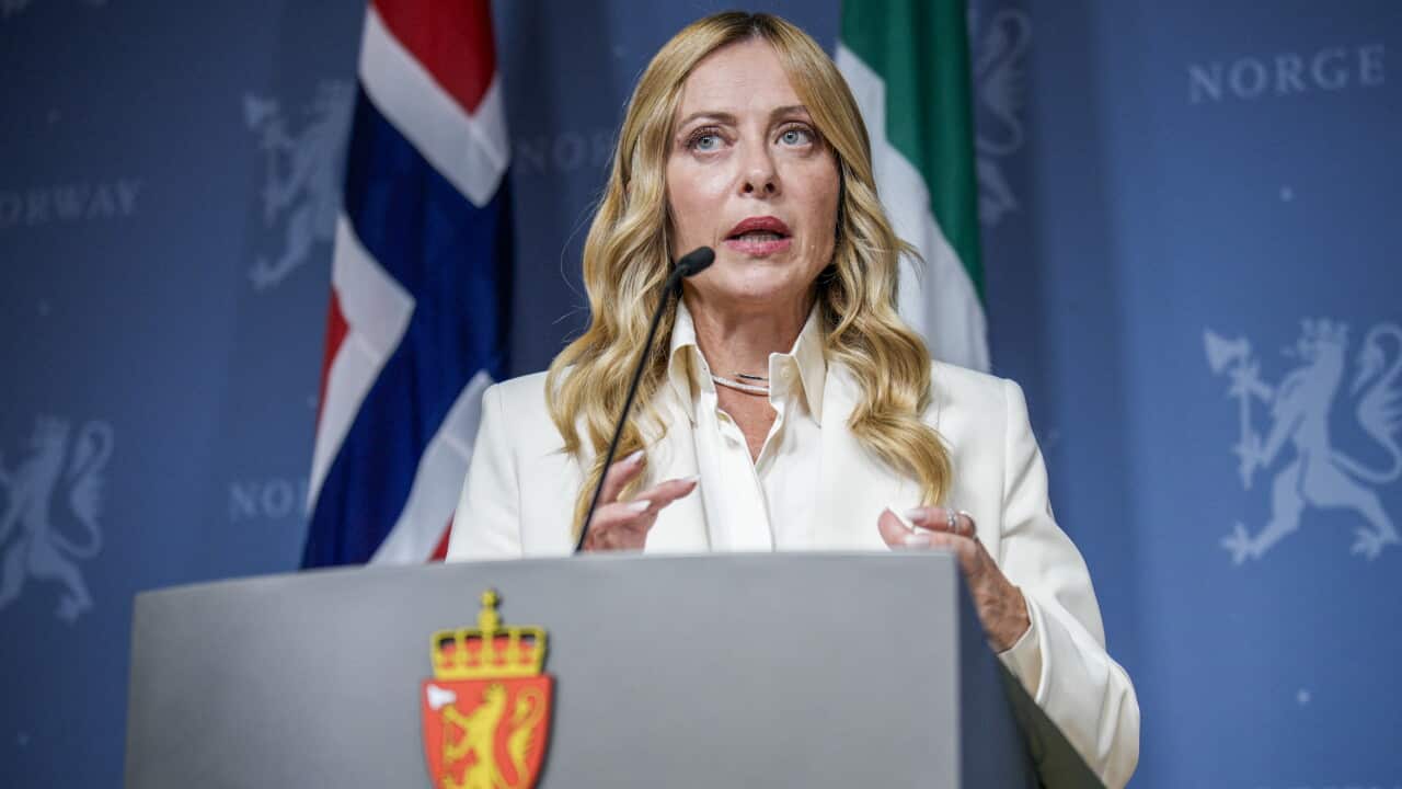 A woman in a white suit speaks at a podium