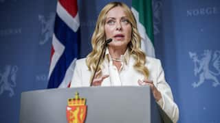 A woman in a white suit speaks at a podium