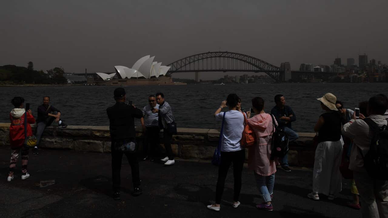 Tourists take photographs against the backdrop of the Sydney Harbour Bridge and the Sydney Opera House as a dust storm descends on Sydney.