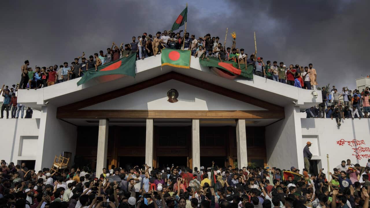 People gather around and on top of the regal residence of the Bangladeshi prime minister in Dhaka. Those on the roof have draped Bangladesh flags - a red circle on top of a dark green background - over the main entrance portico.