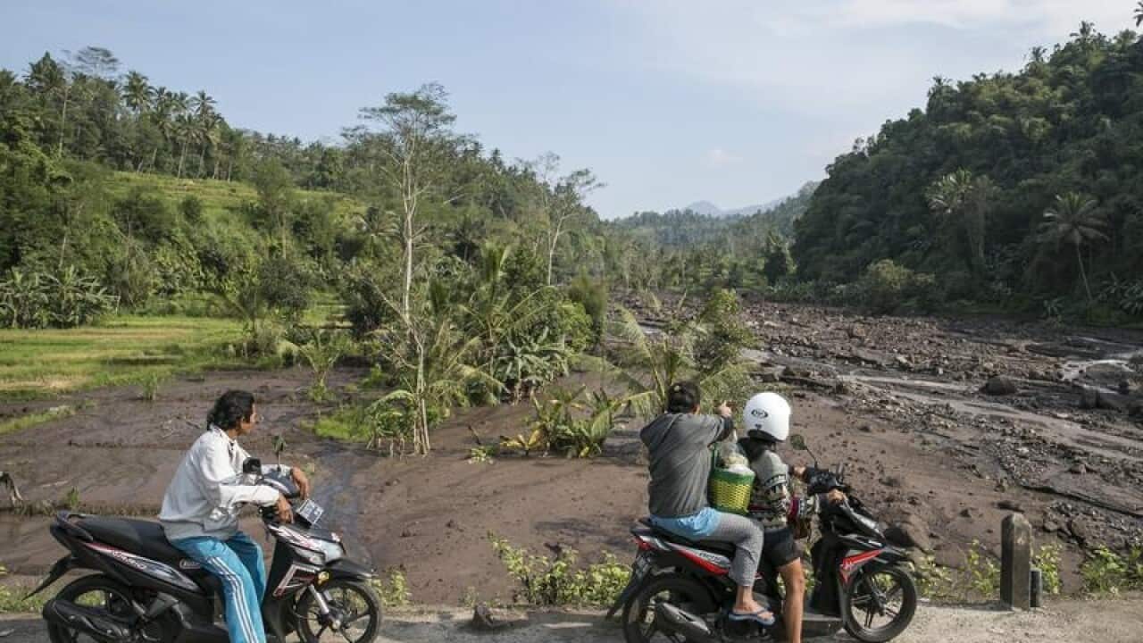 Motorist look at a river overflowing with water and volcanic ash.