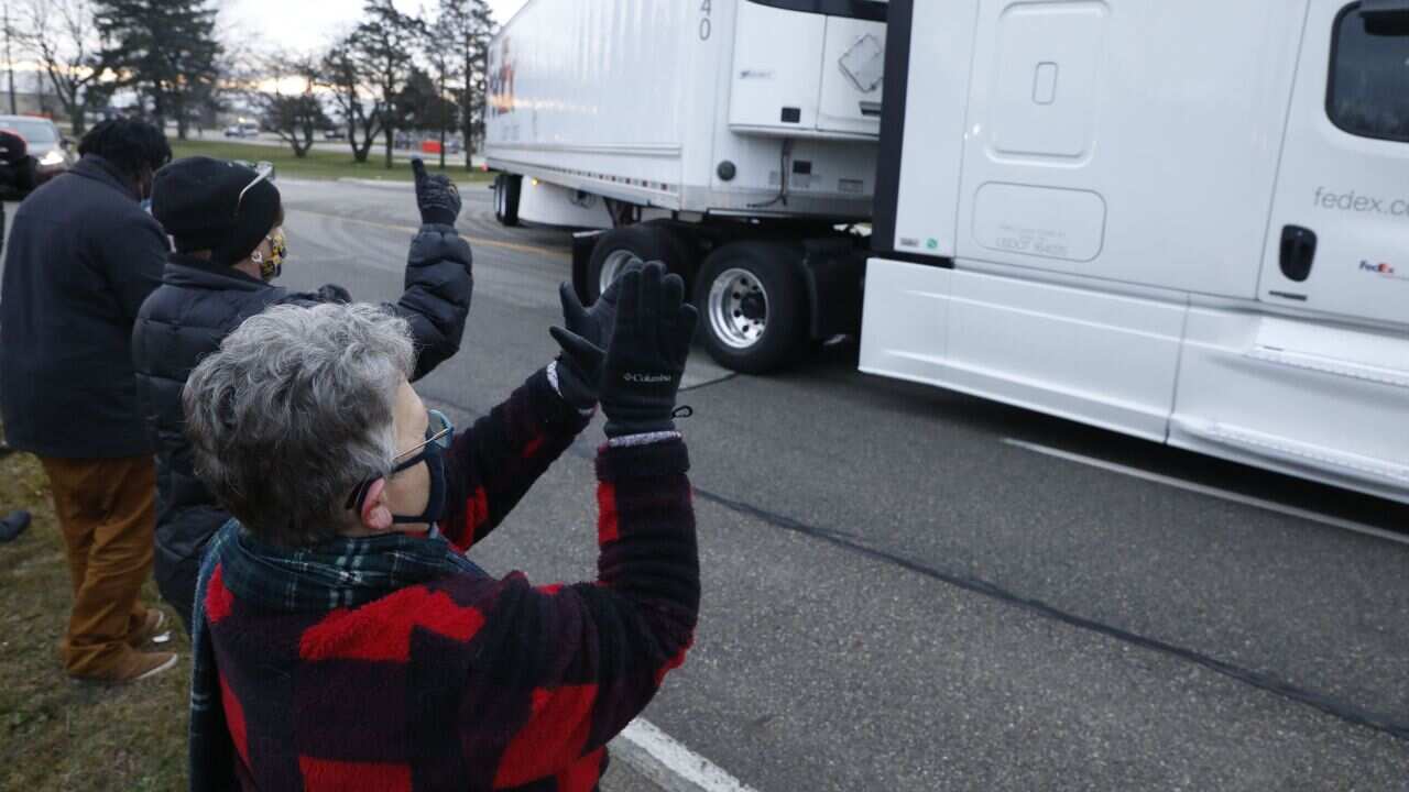 People cheer as trucks carrying the first shipment of the COVID-19 vaccine leaves Pfizer's Global Supply facility in Kalamazoo, Michigan on 13 December, 2020.