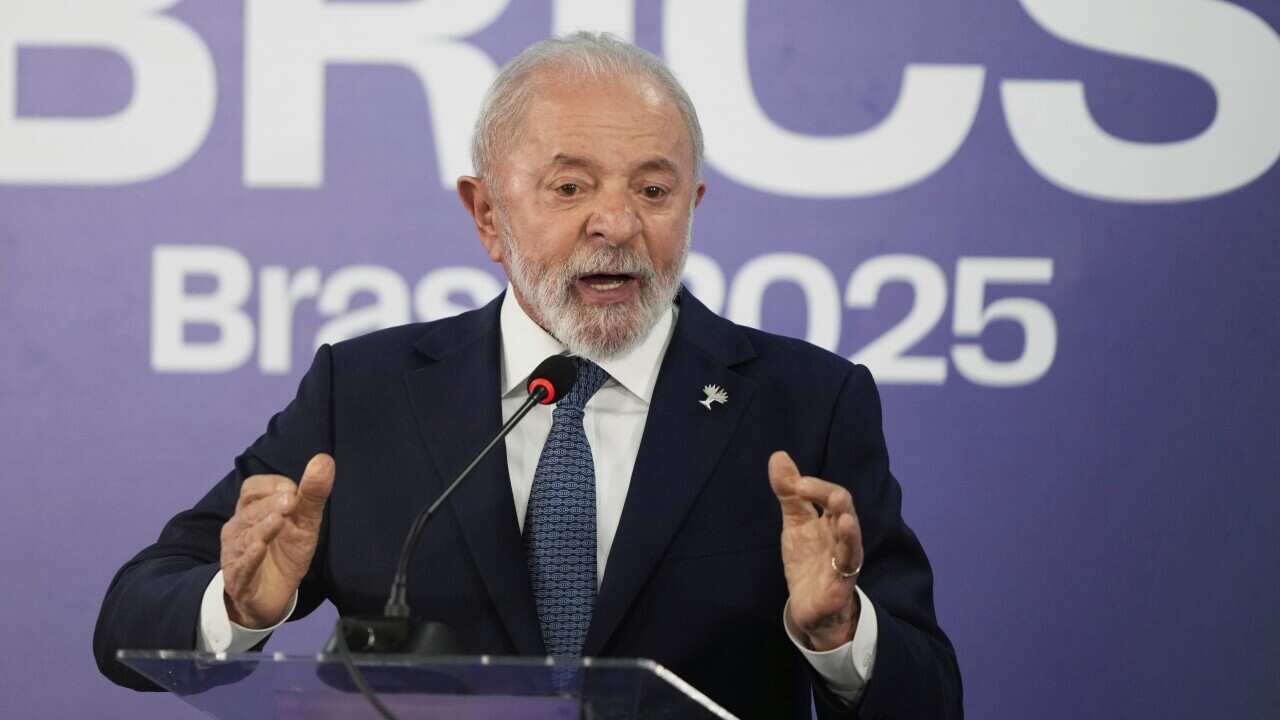 A man wearing a suit at a podium. There is a sign behind him that reads BRICS Brasil 2025