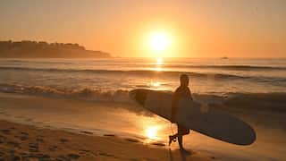 Sunrise over a beach, a man with a surfboard walks past