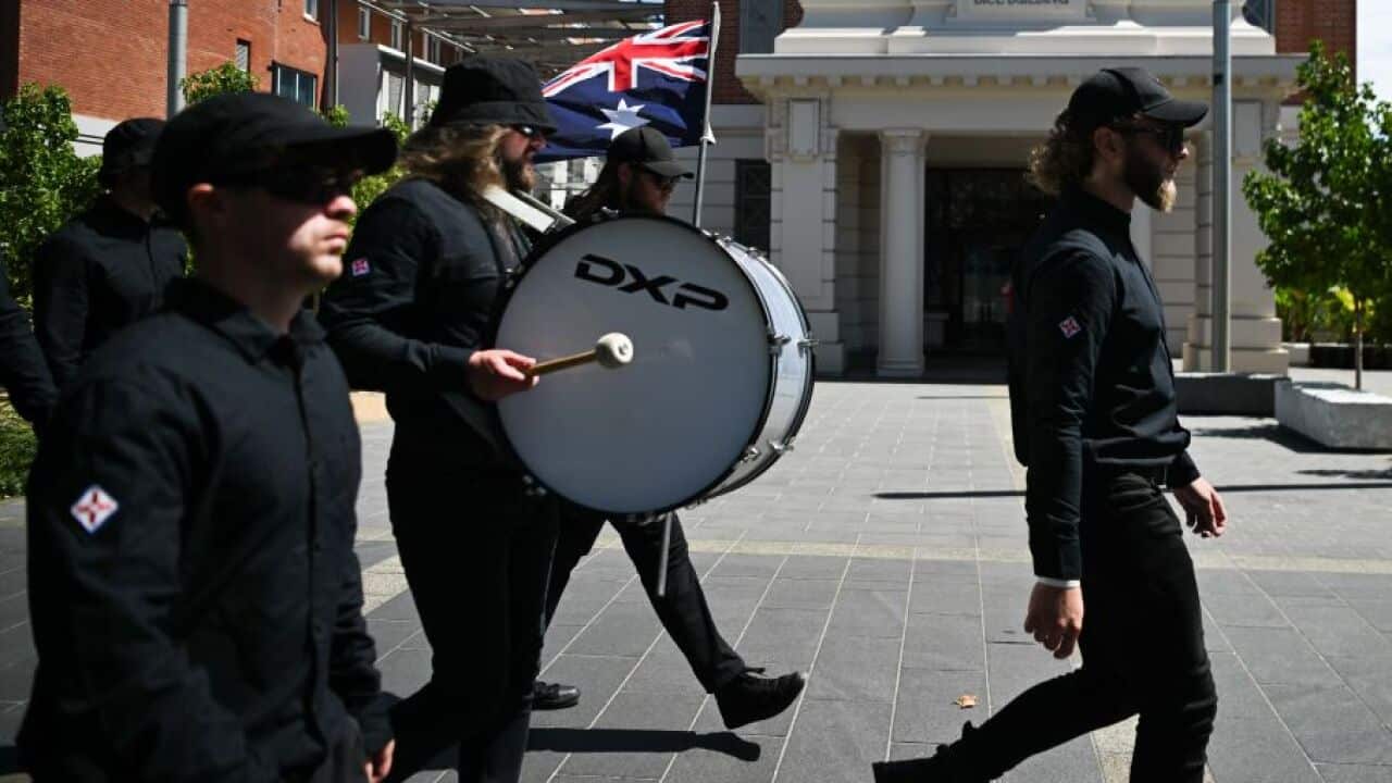 Men dressed in all black marching with a drum and Australian flag