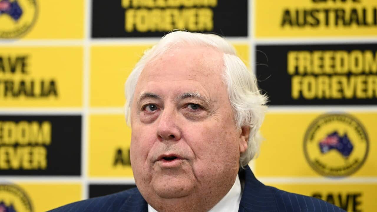 Clive Palmer sitting in front of a row of United Australia Party logos and slogans.