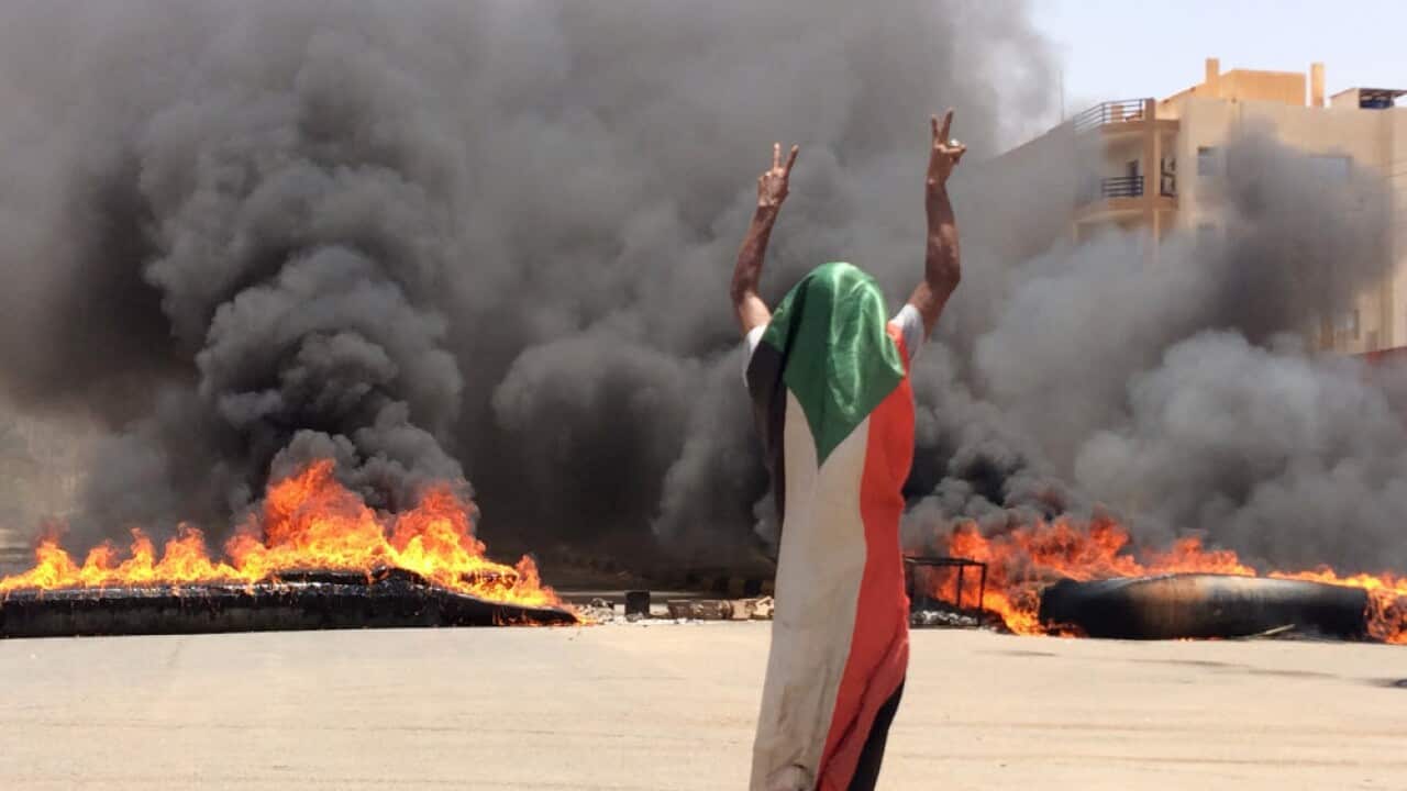 A protester wearing a Sudanese flag in front of burning tires and debris on road 60, near Khartoum's army headquarters