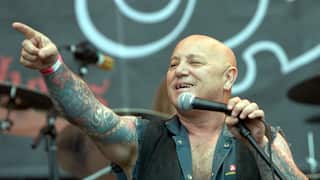 A man points at something while holding a microphone as he performs on a stage