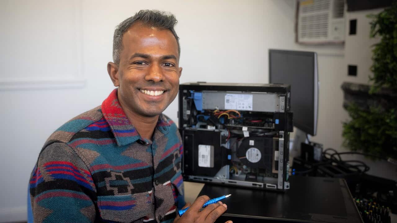 A man in a multi-coloured jacket sitting next to a computer.