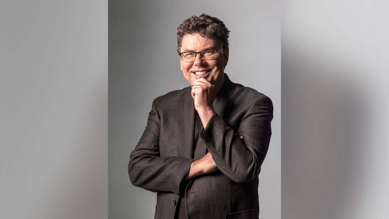 A man wearing a suit and glasses smiles and poses for a photo