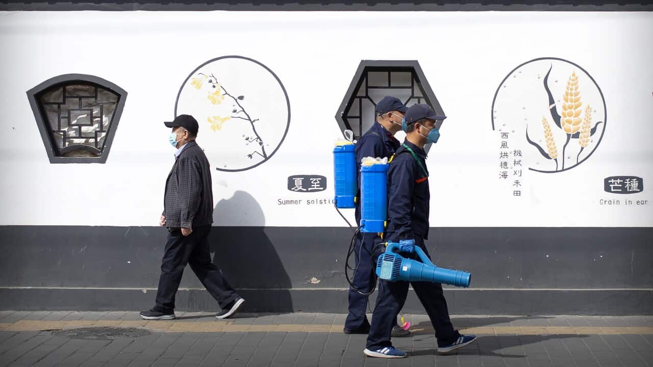 Workers wearing face masks and carrying disinfectant sprayers walk along a street in Beijing.
