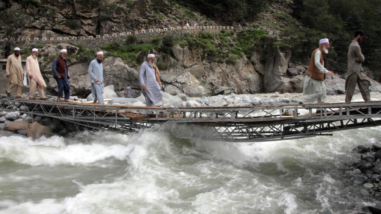 People risking their lives crossing a raging river on a bridge damaged by floodwaters