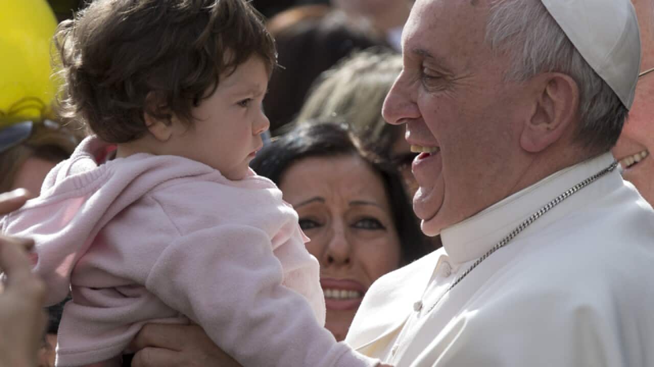 Pope Francis smiles as he holds a baby