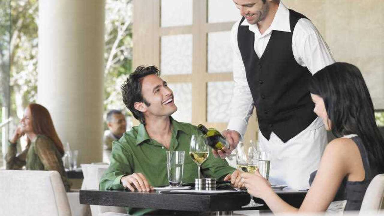 Waiter pouring wine for couple at outdoor restaurant.