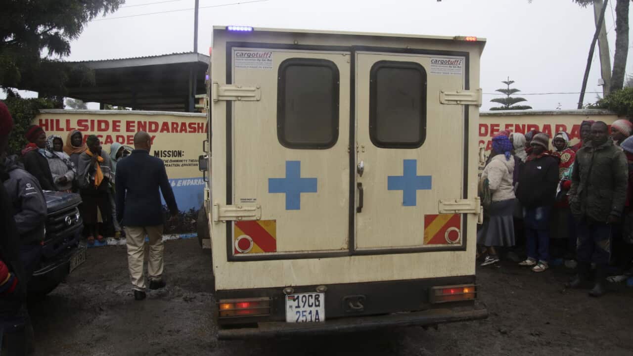 An ambulance parked on a dirt road outside a building surrounded by people.