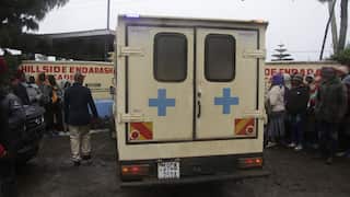 An ambulance parked on a dirt road outside a building surrounded by people.