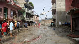 People walk through mud in a flooded street, a helicopter flies in the distance