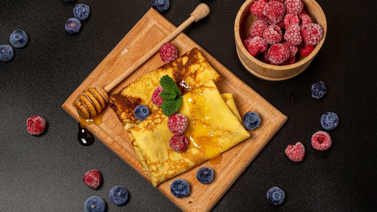 Top view, thin pancakes with berries, mint leaves and honey, dark background