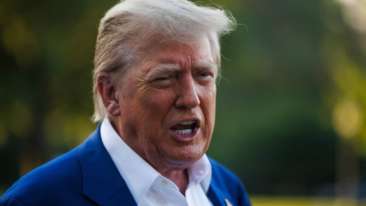 Donald Trump, wearing a blue suit, is speaking while standing outside.